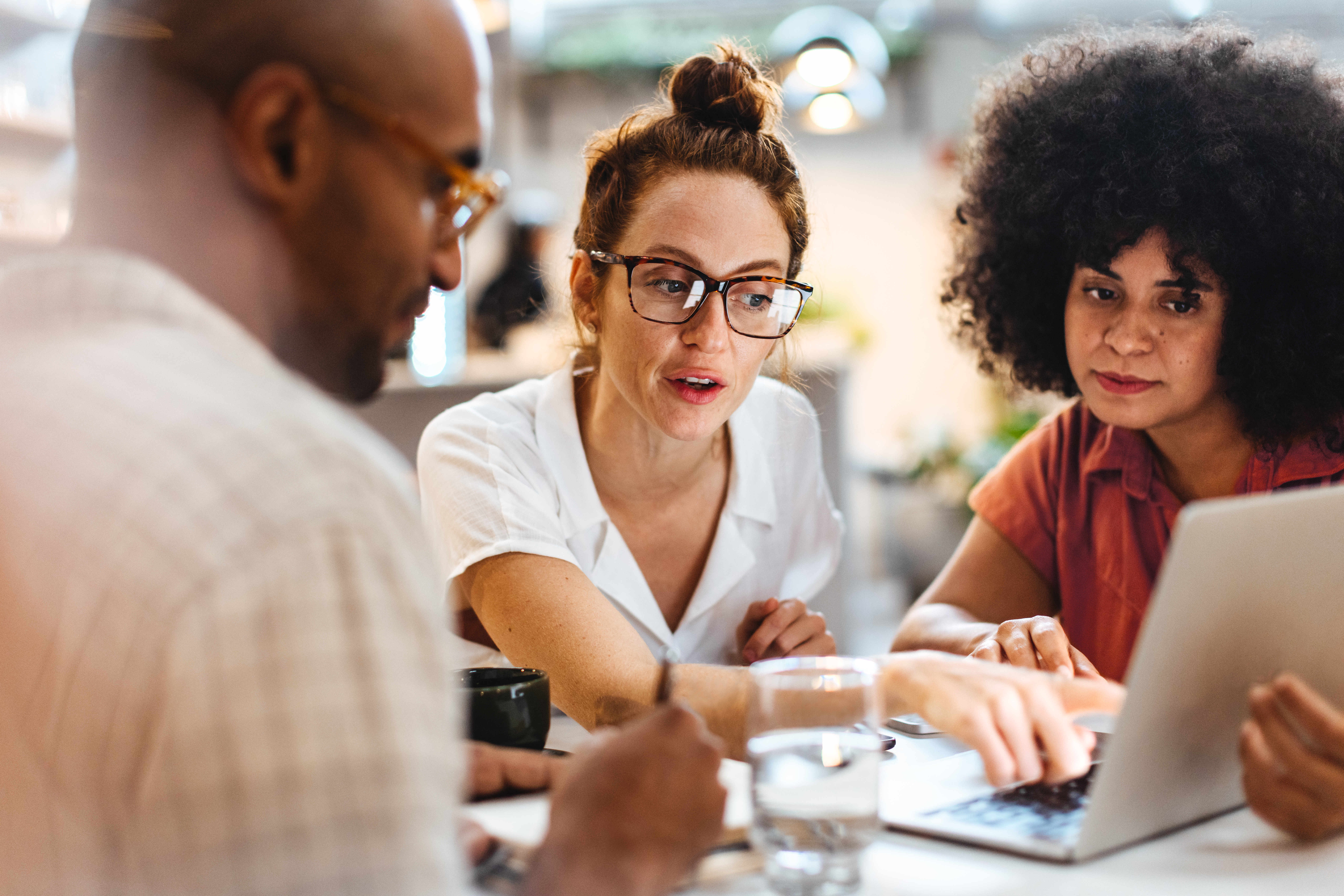 Business women having a work lunch in a café, exchanging ideas and discussing their projects with a coworker. Young business team using a laptop as they sit around a coffee table.